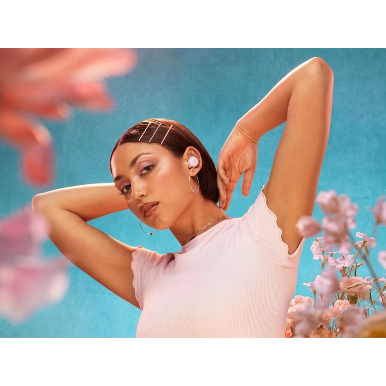 Eine Frau mit Ohrhörern und rosa Oberteil posiert vor blauem Hintergrund mit Blumen.