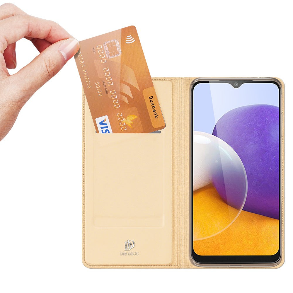 Una mano inserisce una carta di credito dorata in una custodia gialla per telefono accanto a un telefono.