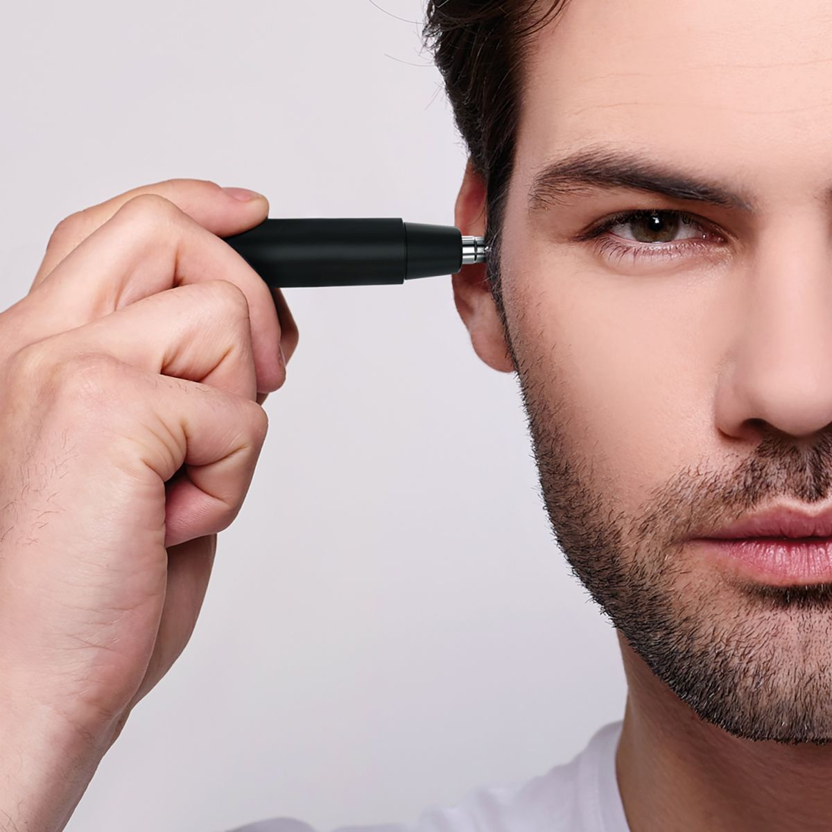 Mężczyzna używa czarnej maszynki do włosów w uchu.