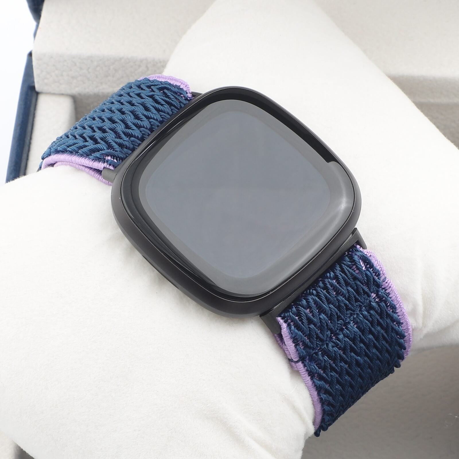 Un écran carré de montre connectée avec un bracelet en tissu bleu à accents violets.