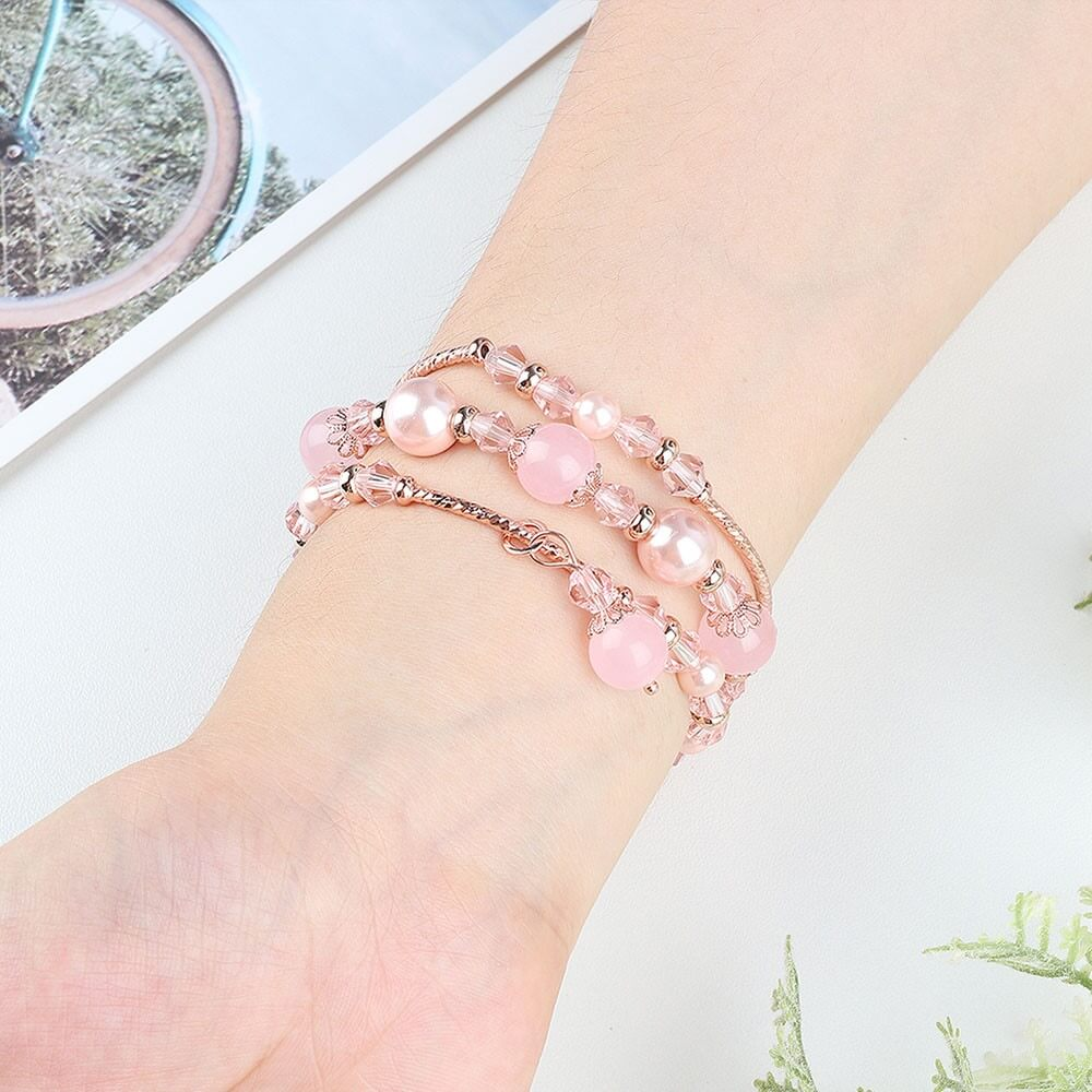 Un bracelet de perles roses et de perles de cristal enroulé autour d'un poignet.