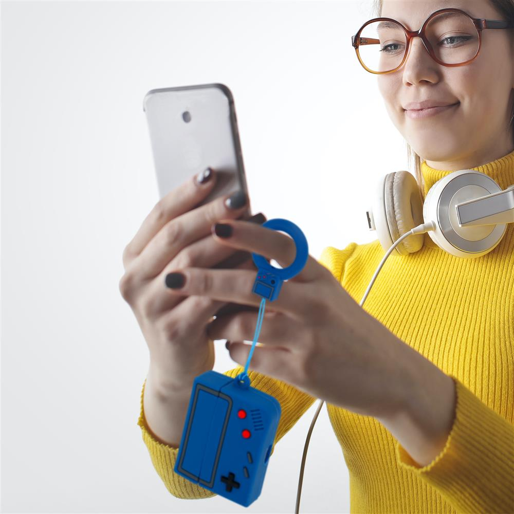 Frau mit Kopfhörern und Brille hält Handy mit Gameboy-Schlüsselanhänger.