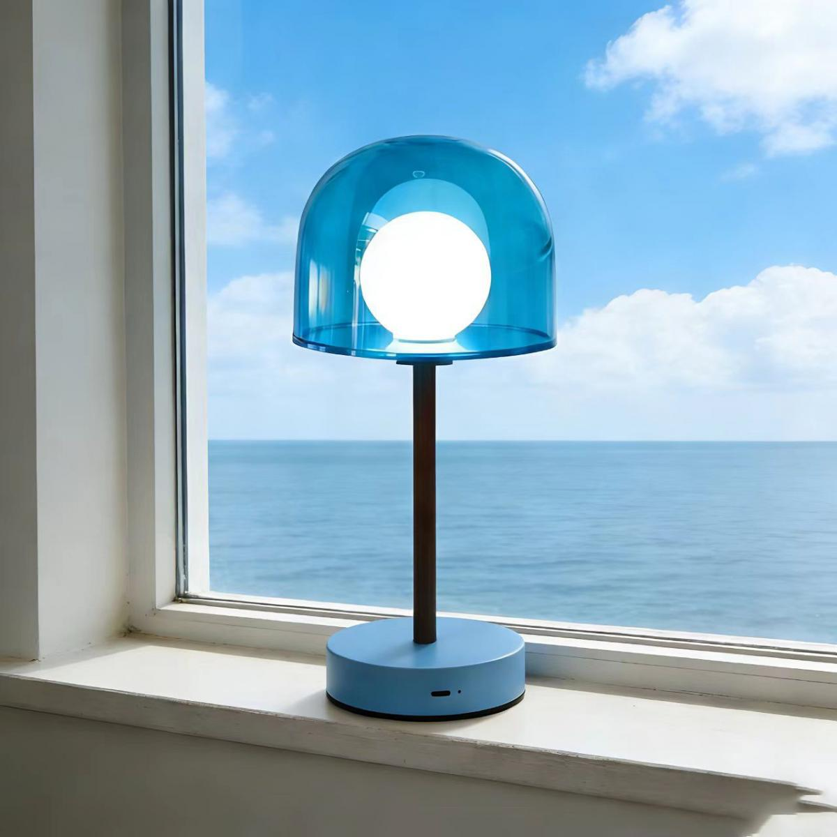 Eine blaue Lampe steht auf einem Fensterbrett mit Blick auf das Meer und den Himmel.