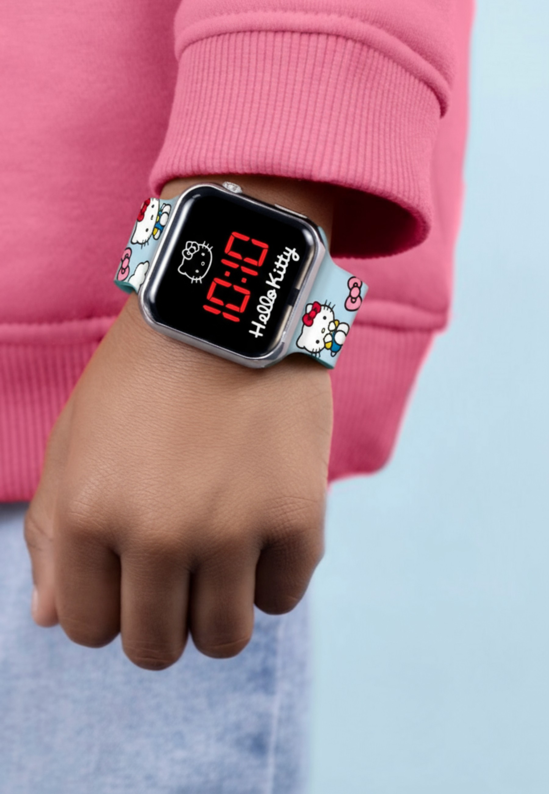 Eine Hand trägt eine rosa Kapuzenpullover und eine Hello Kitty Uhr.