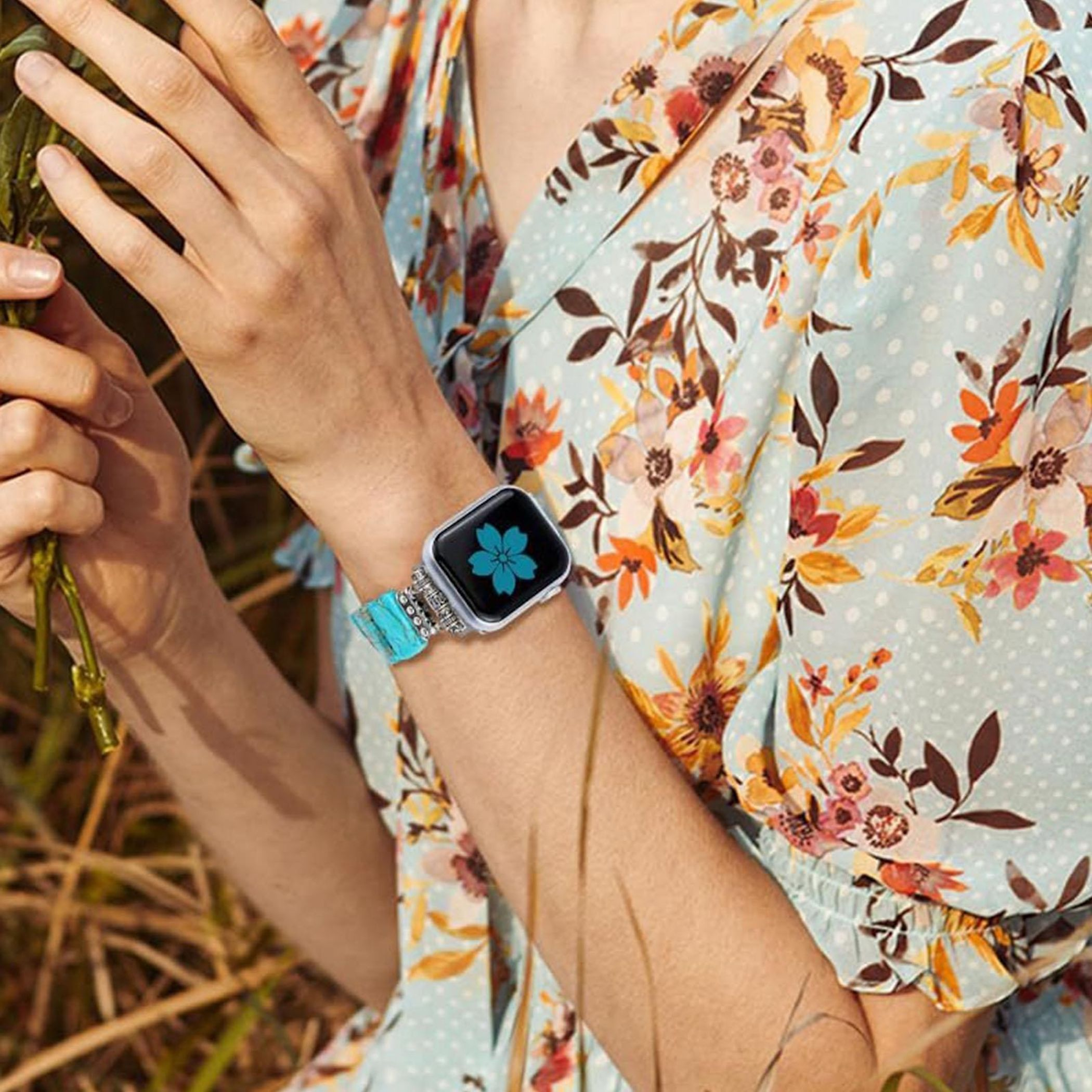 Arm mit Smartwatch und blauem Blumen-Zifferblatt, trägt ein geblümtes Kleid.