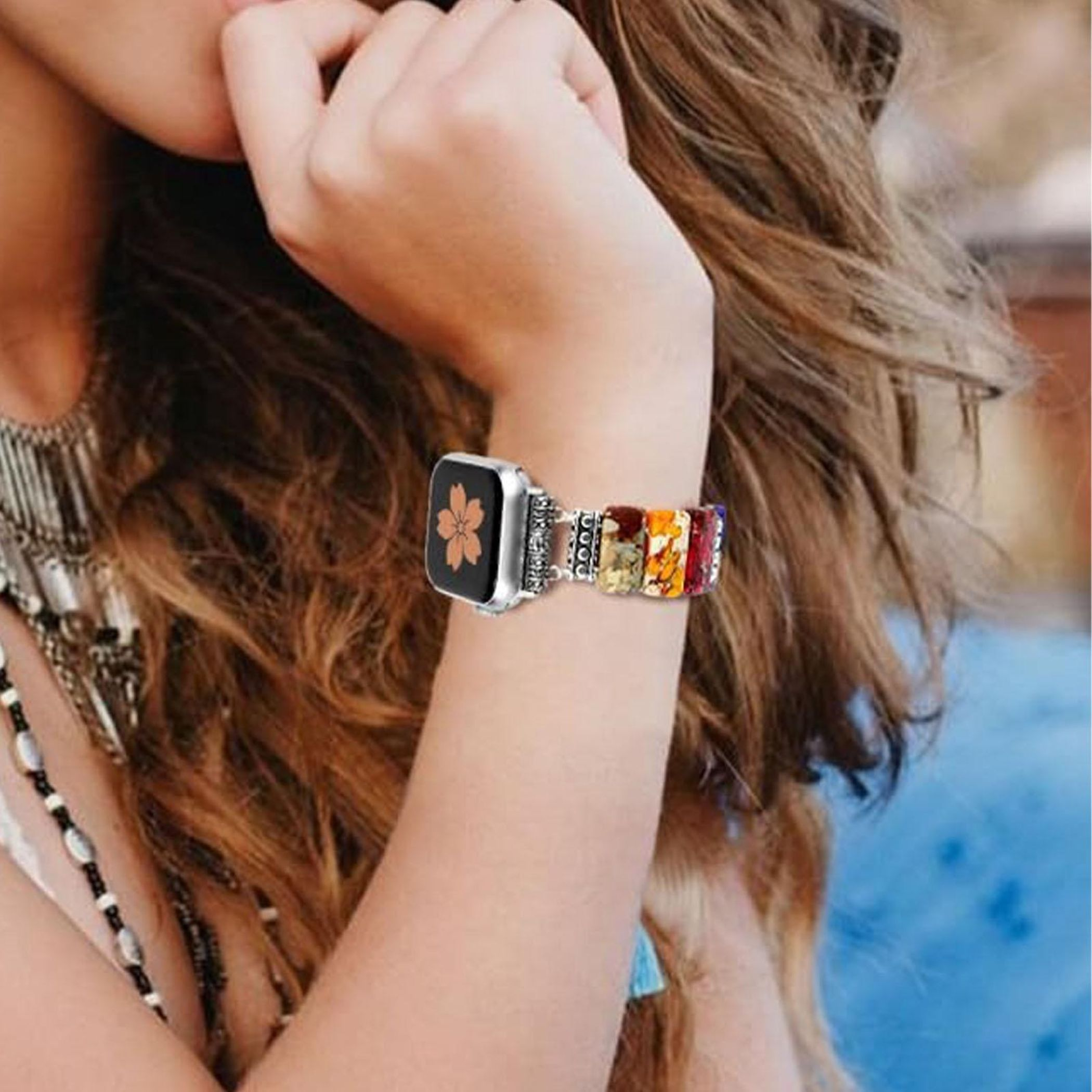 Eine Frau trägt eine Smartwatch mit einem blumenförmigen Zifferblatt und einem bunten Perlenarmband.