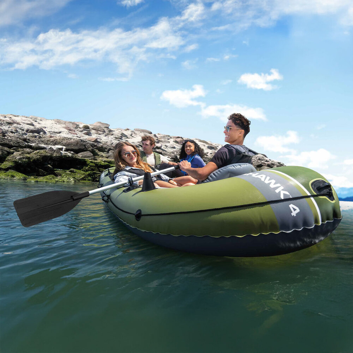 Vier Personen in einem grünen Schlauchboot auf dem Wasser, im Hintergrund Felsen.