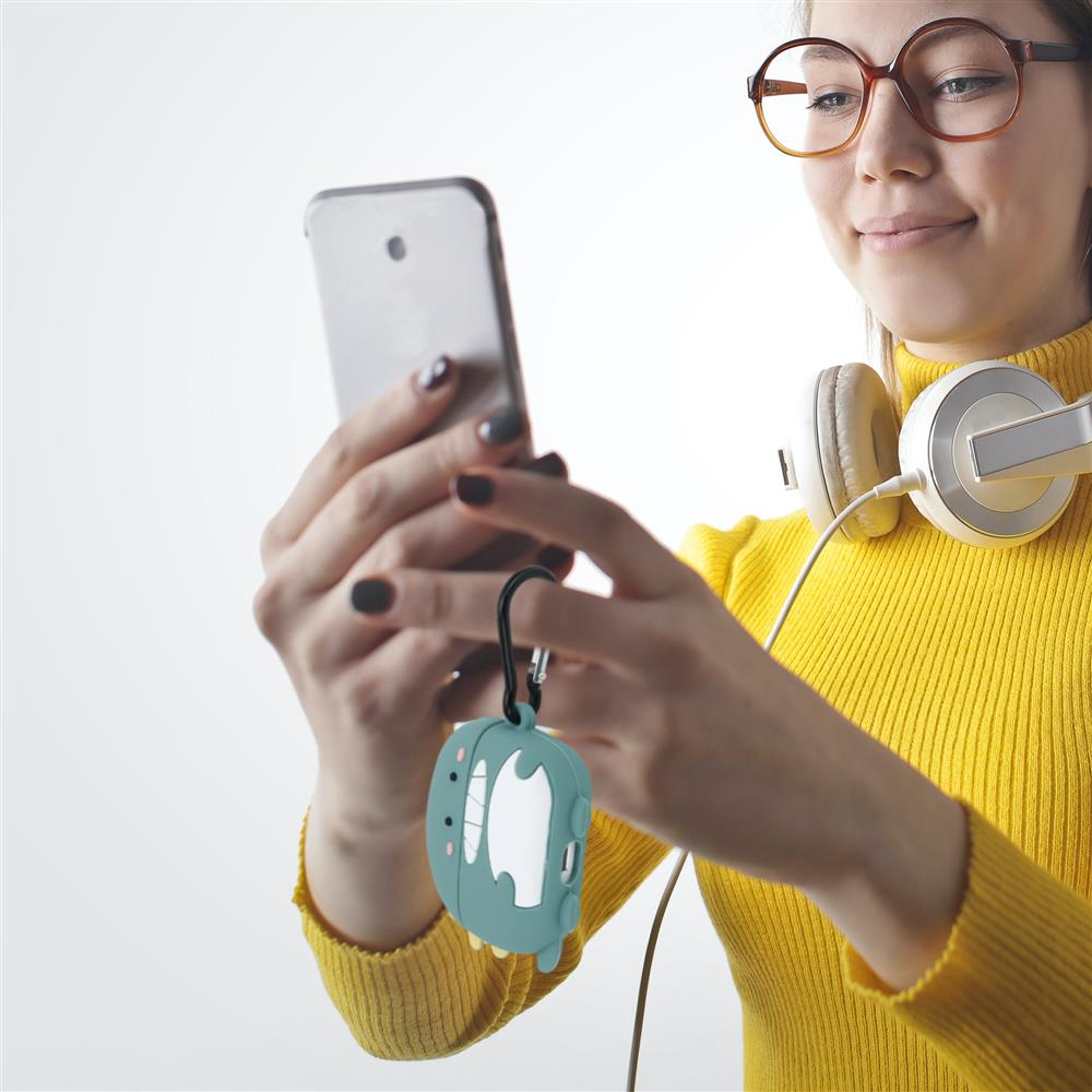 Eine Frau mit Brille und Kopfhörern hält ein Smartphone und einen Dino-Anhänger.