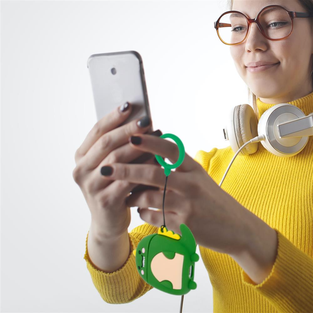 Eine Frau mit Brille und Kopfhörern hält ein Smartphone und einen grünen Dinosaurier-Schlüsselanhänger.
