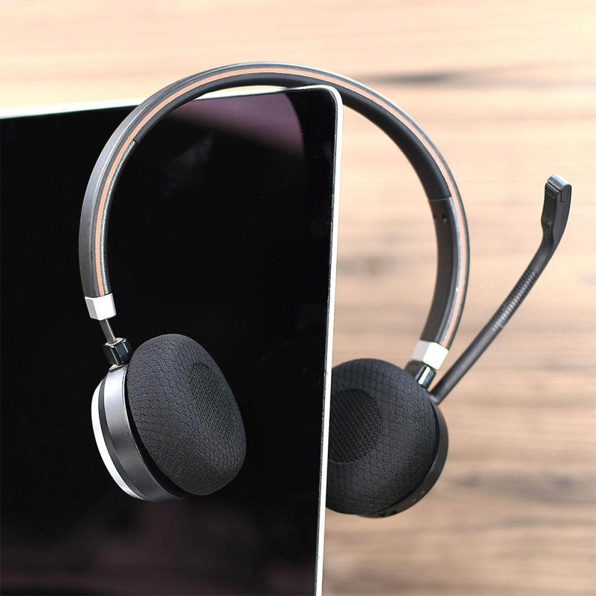 Un auricolare nero con microfono poggia contro lo schermo di un tablet su un tavolo.