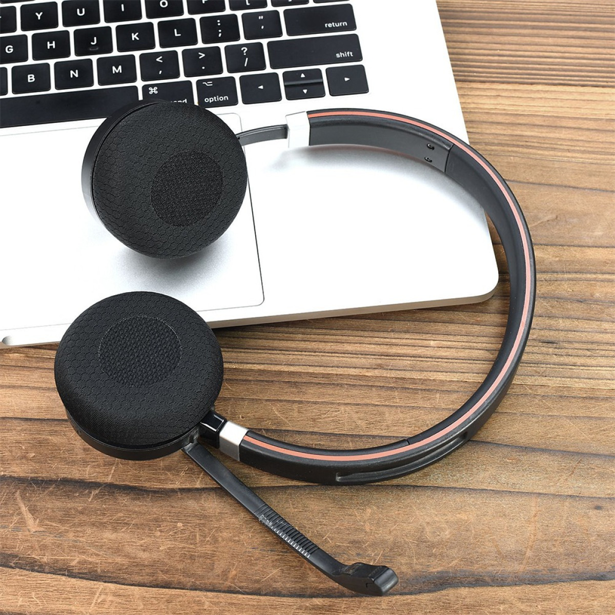 Cuffie nere con microfono appoggiate sulla tastiera di un laptop e tavolo in legno.