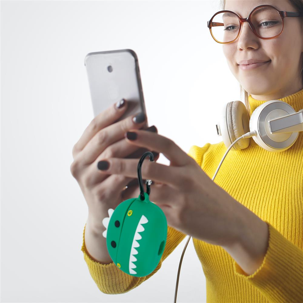 Eine Frau mit Brille und Kopfhörern hält ein Smartphone und einen grünen Dinosaurier-Schlüsselanhänger.