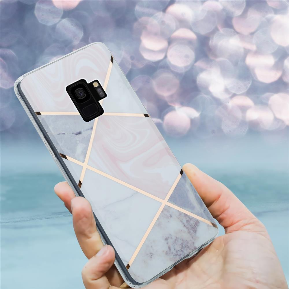 Una mano tiene uno smartphone con motivo marmo e linee dorate.