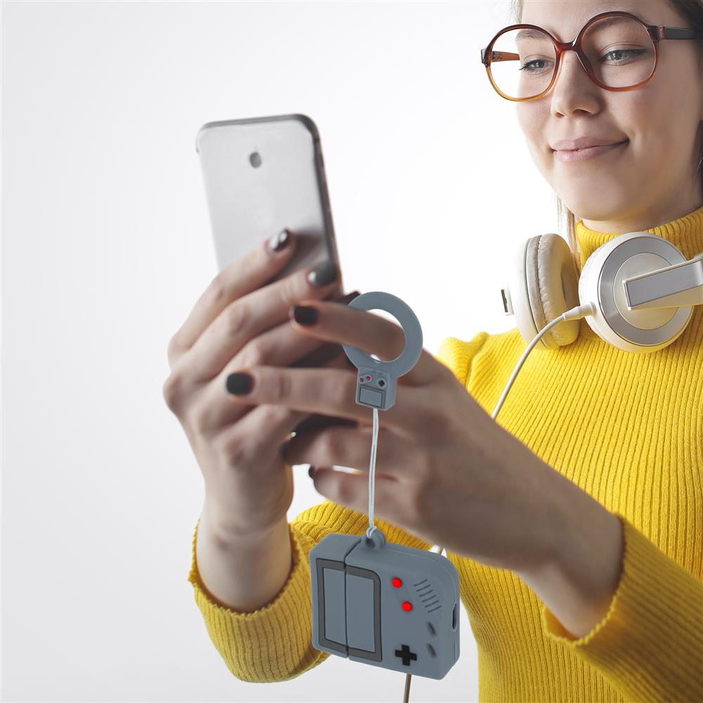Eine Frau mit Brille und Kopfhörern hält ein Smartphone. Ein grauer Anhänger im Stil eines Gameboys hängt.