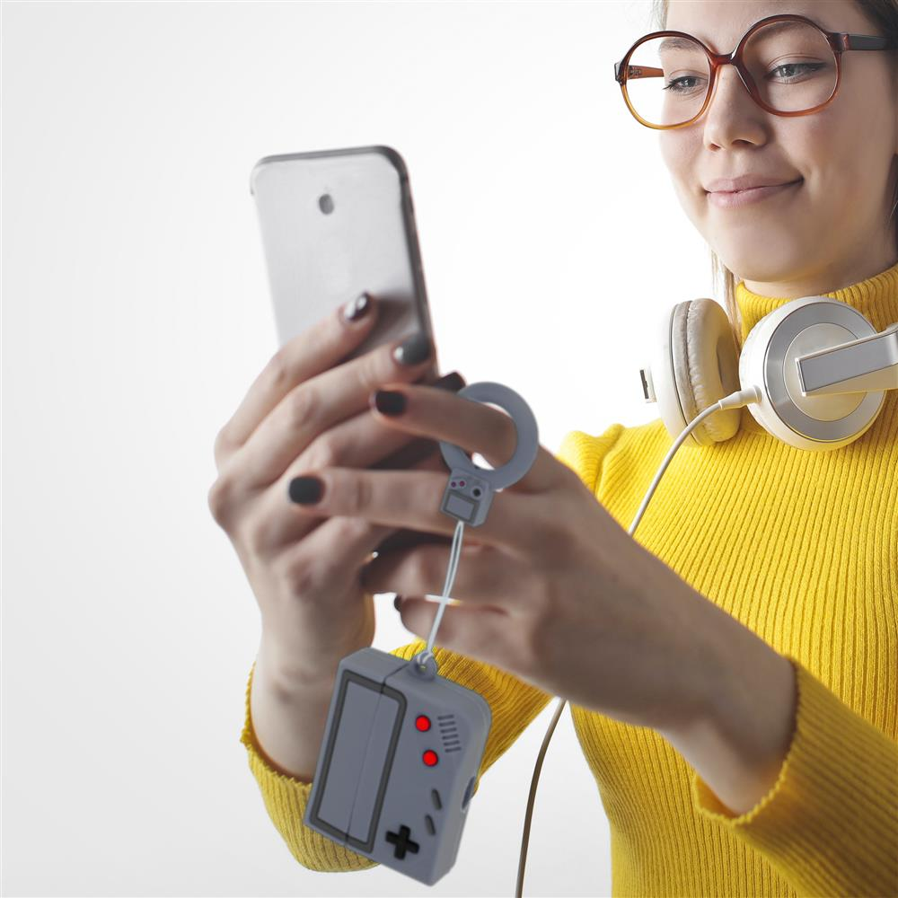 Eine Frau mit Brille und Kopfhörern hält ein Smartphone mit einem Gamecontroller-Schlüsselanhänger.