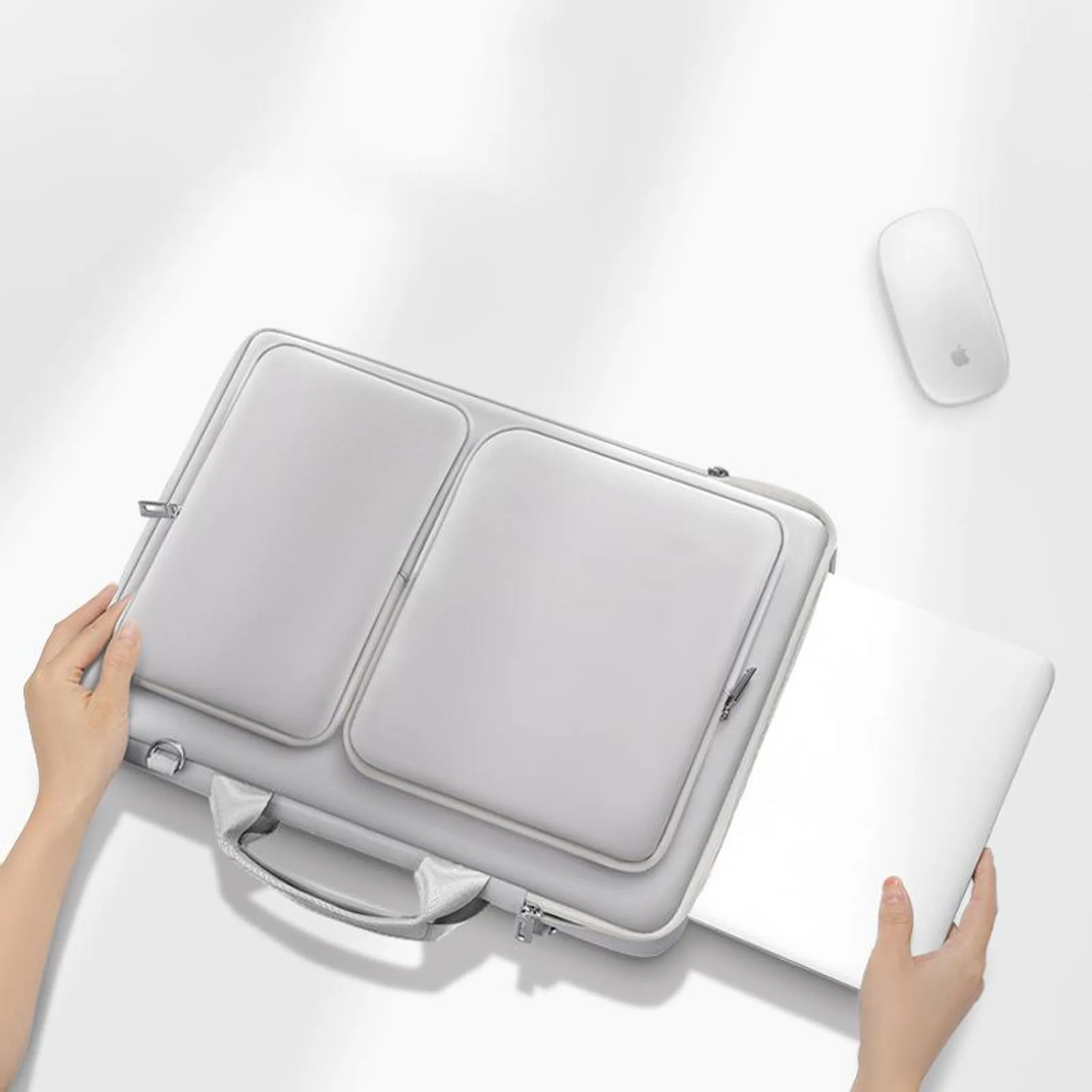 Graue Laptoptasche mit zwei Fächern, Laptop wird eingesetzt, weiße Maus daneben.
