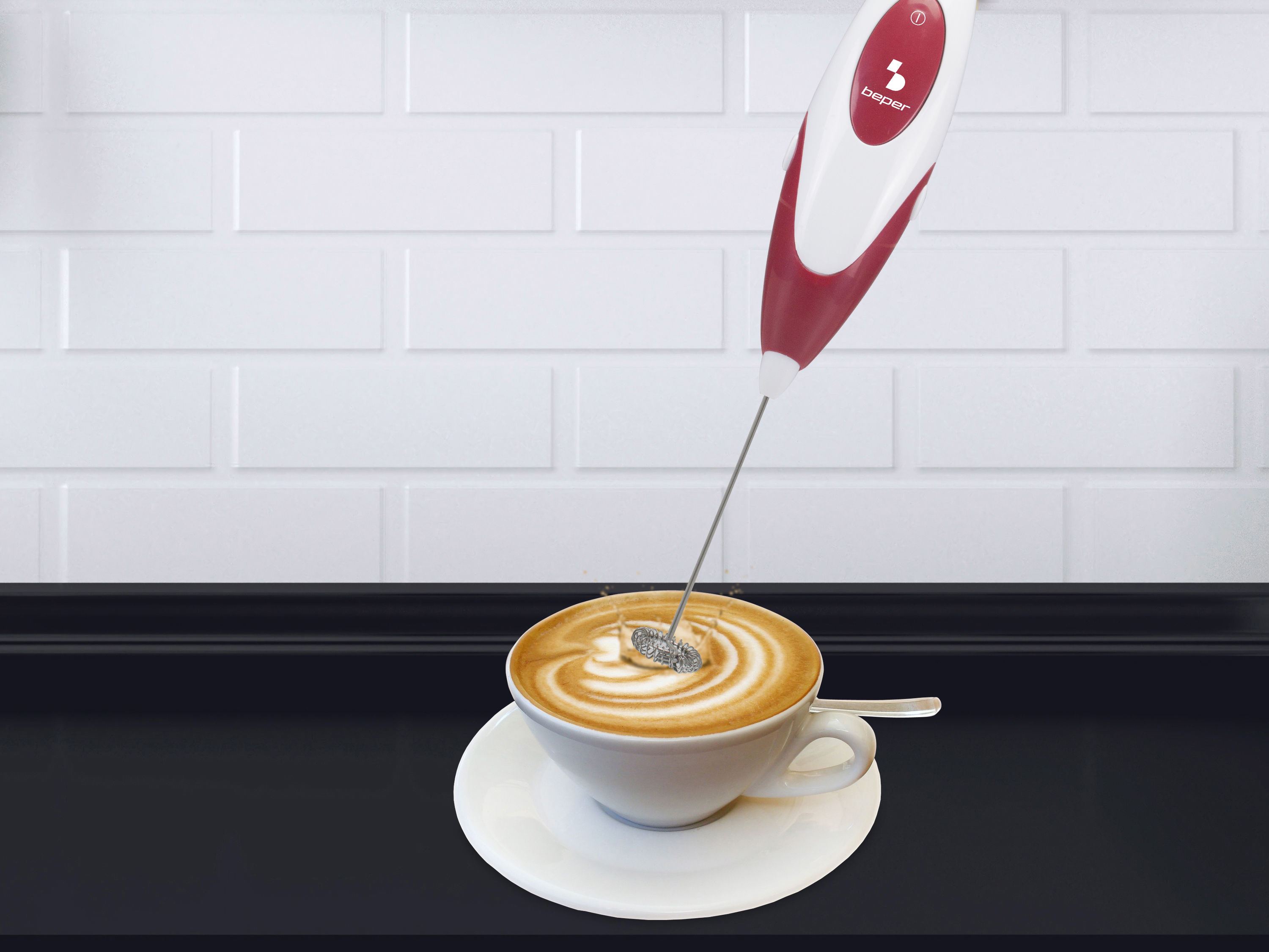 Un montalatte rosso e bianco sopra una tazza di latte art su un piattino bianco.