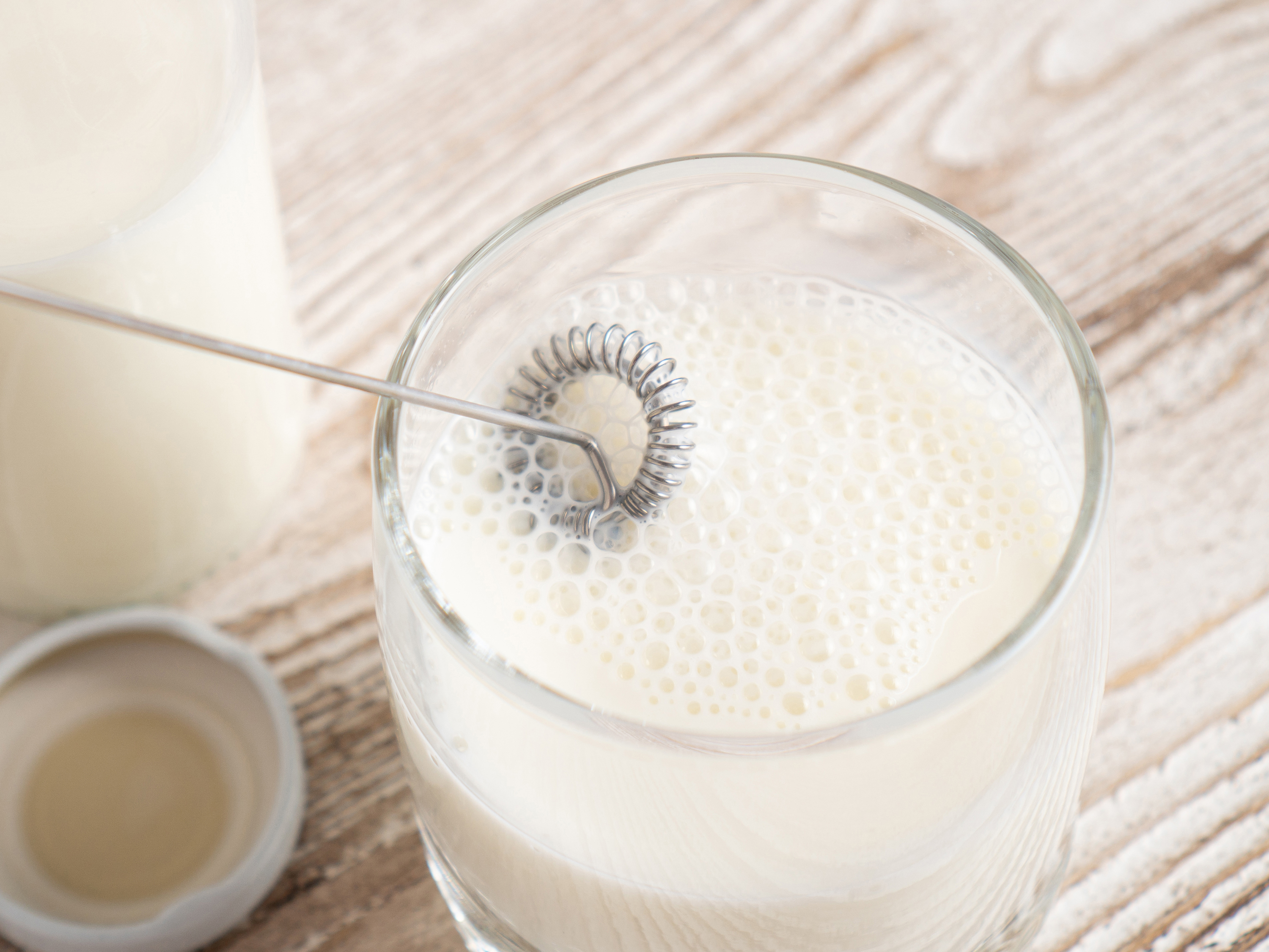 Il latte viene montato in un bicchiere con una frusta. Una caraffa di latte è accanto.
