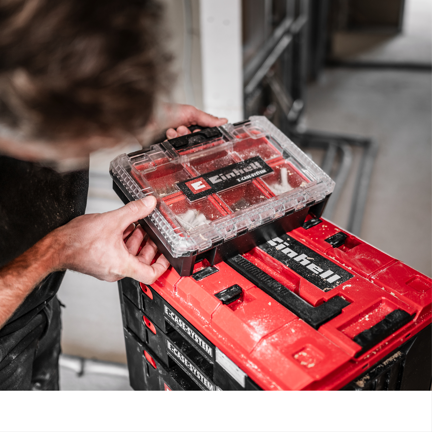 Ein Mann platziert einen durchsichtigen Werkzeugkasten auf roten Stapelboxen.