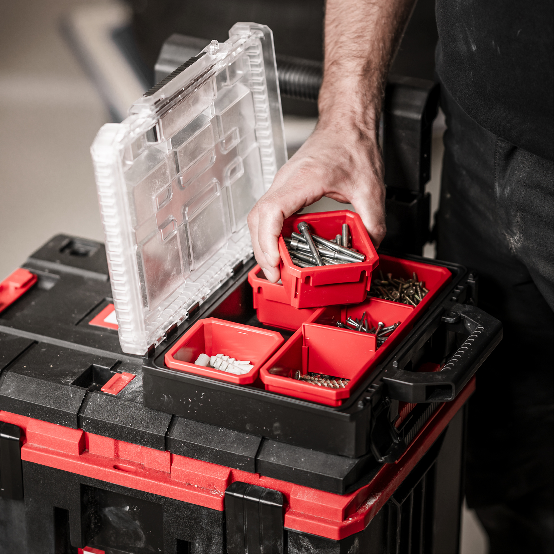 Hand nimmt rote Box mit Schrauben aus schwarzer Werkzeugkiste.