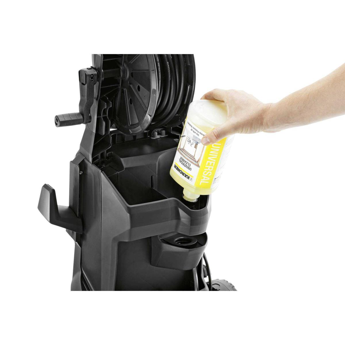 A hand pours yellow liquid from a bottle into a pressure washer tank.