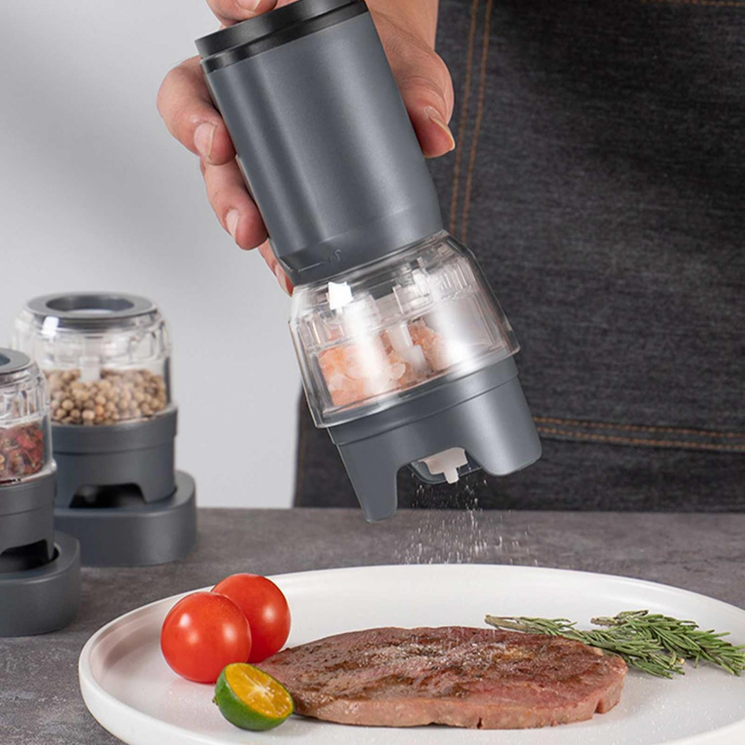 Elektrische Mühle mahlt Gewürze über ein Steak, Tomaten und Limettenspalte.