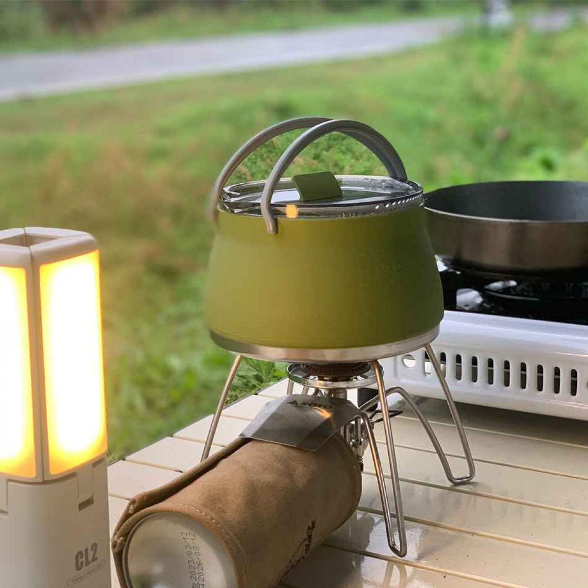 Grüne Teekanne auf Campingkocher neben leuchtender Lampe.