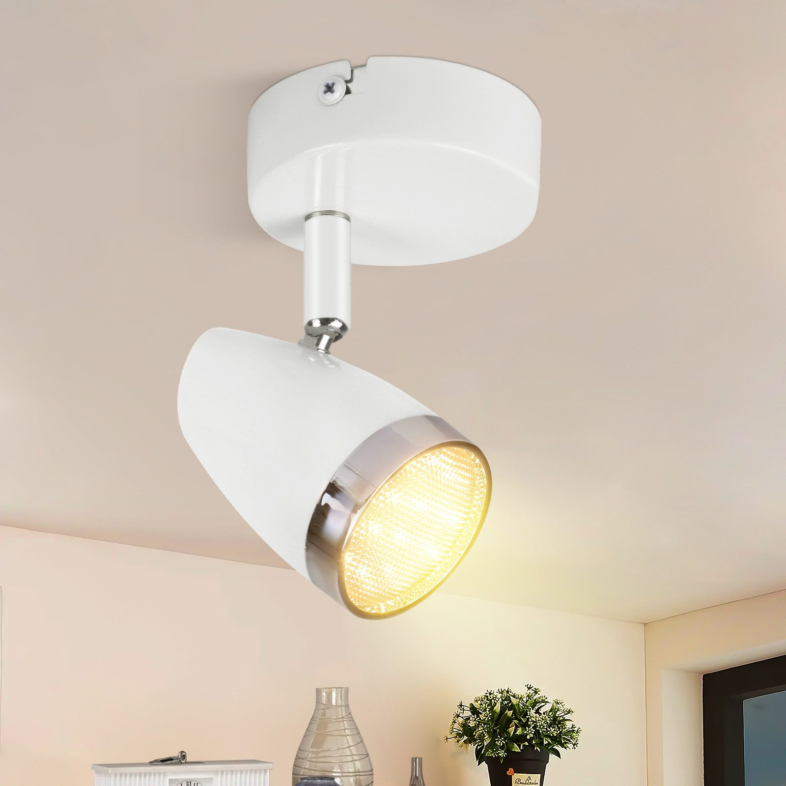 Un faretto da soffitto bianco con anello argentato e lampadina brilla di giallo.