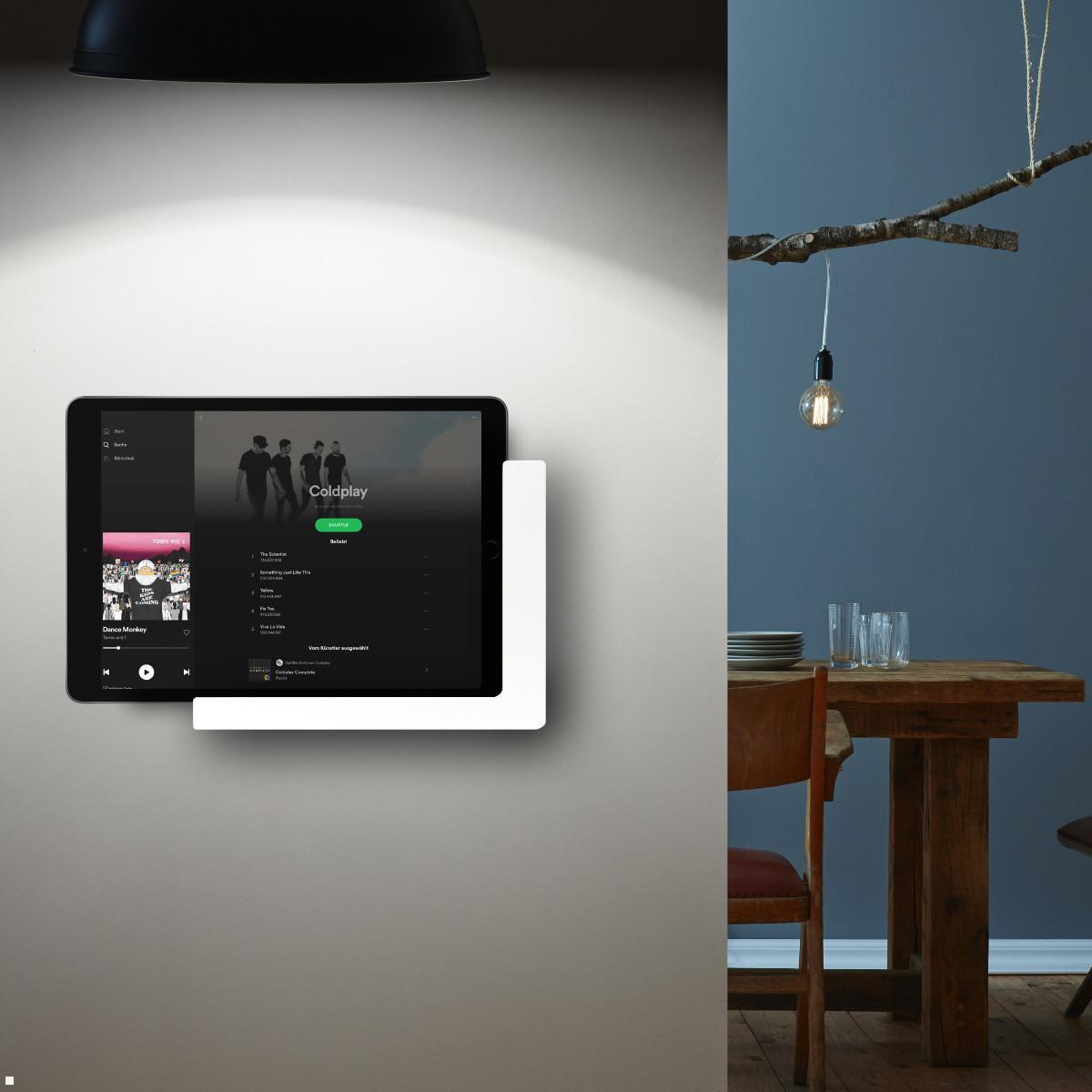 Tablet zeigt Coldplay-Album auf einer Wandhalterung neben einem Holztisch.