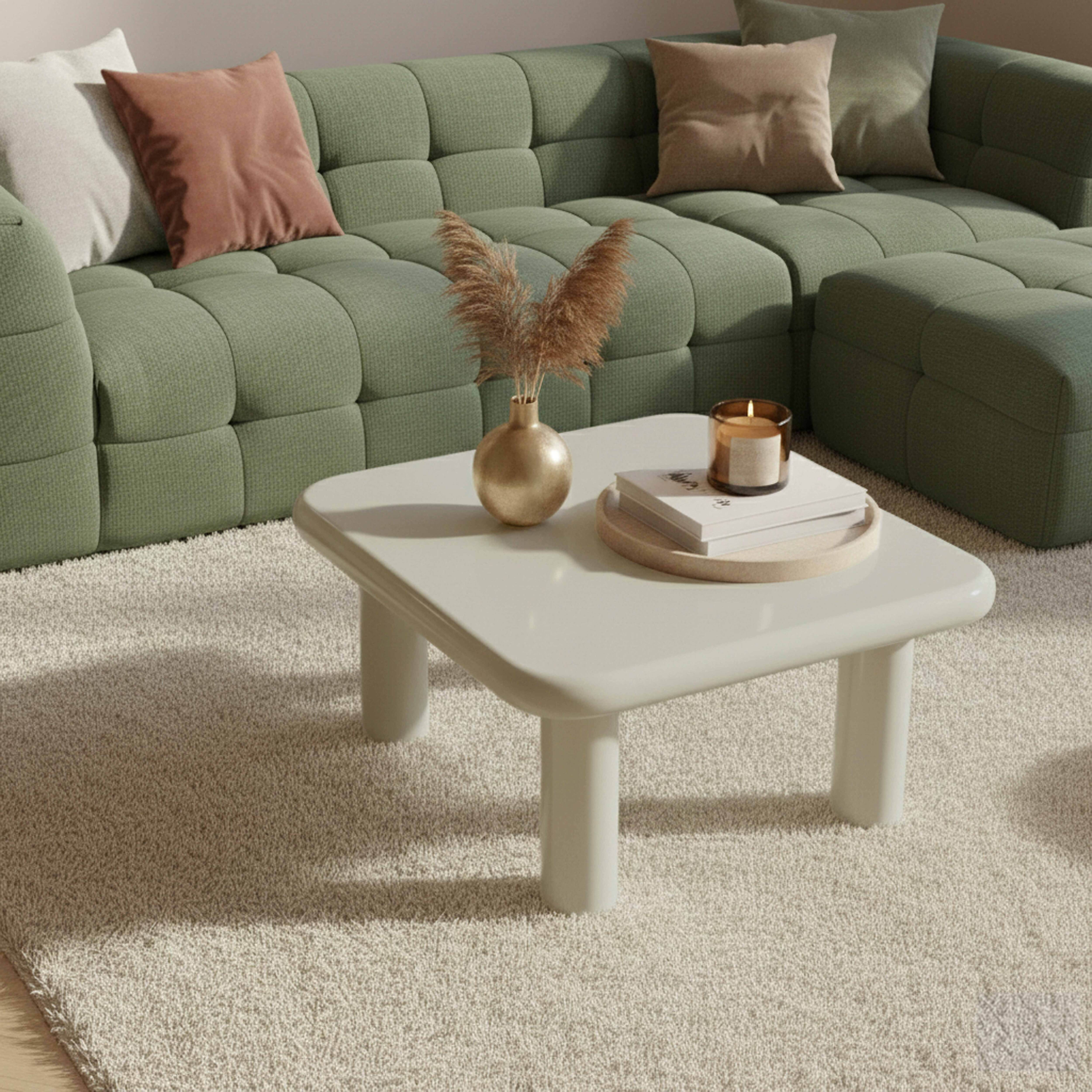 Ein grünes Sofa mit Kissen, ein weißer Couchtisch mit Vase und Kerze.