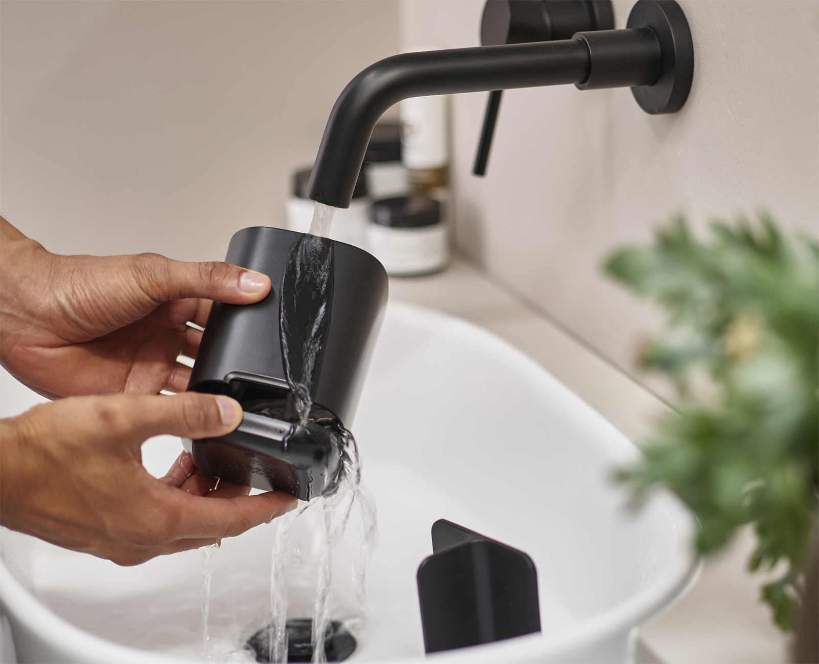 Manos enjuagando un recipiente negro bajo un grifo en un lavabo.