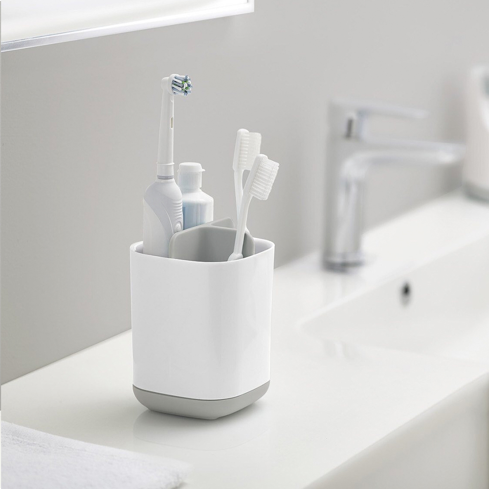 Un soporte blanco con un cepillo de dientes eléctrico y dos manuales, y pasta de dientes.