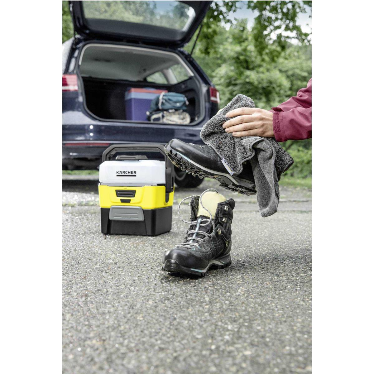 Persona che asciuga uno scarpone da trekking con panno grigio vicino a Karcher e auto.