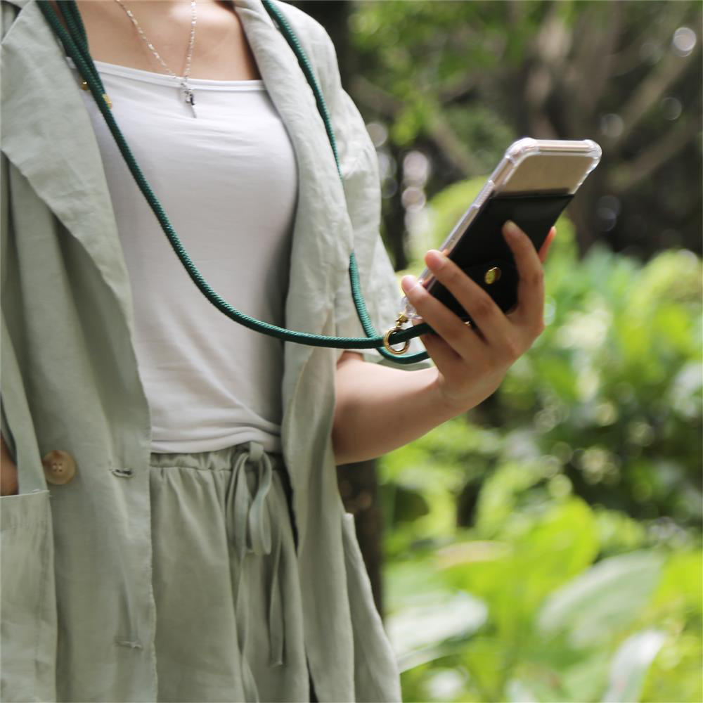 Una persona tiene uno smartphone con cordino verde, circondata dal verde.