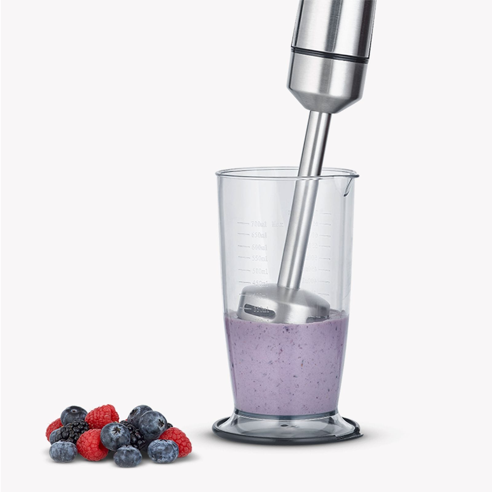 Ein Stabmixer mixt Beeren in einem Messbecher. Beeren liegen daneben.