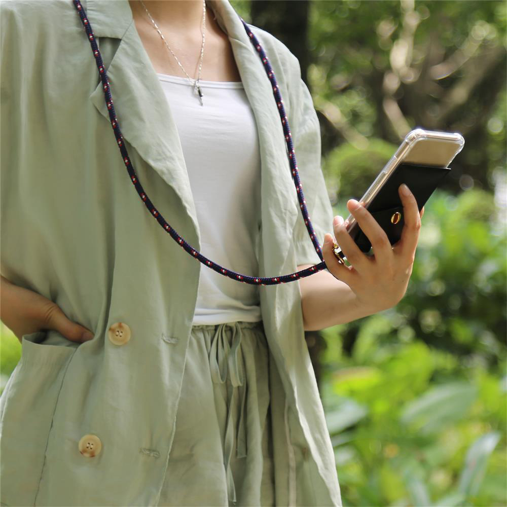 Persona in outfit verde chiaro tiene un telefono con cordino al collo.