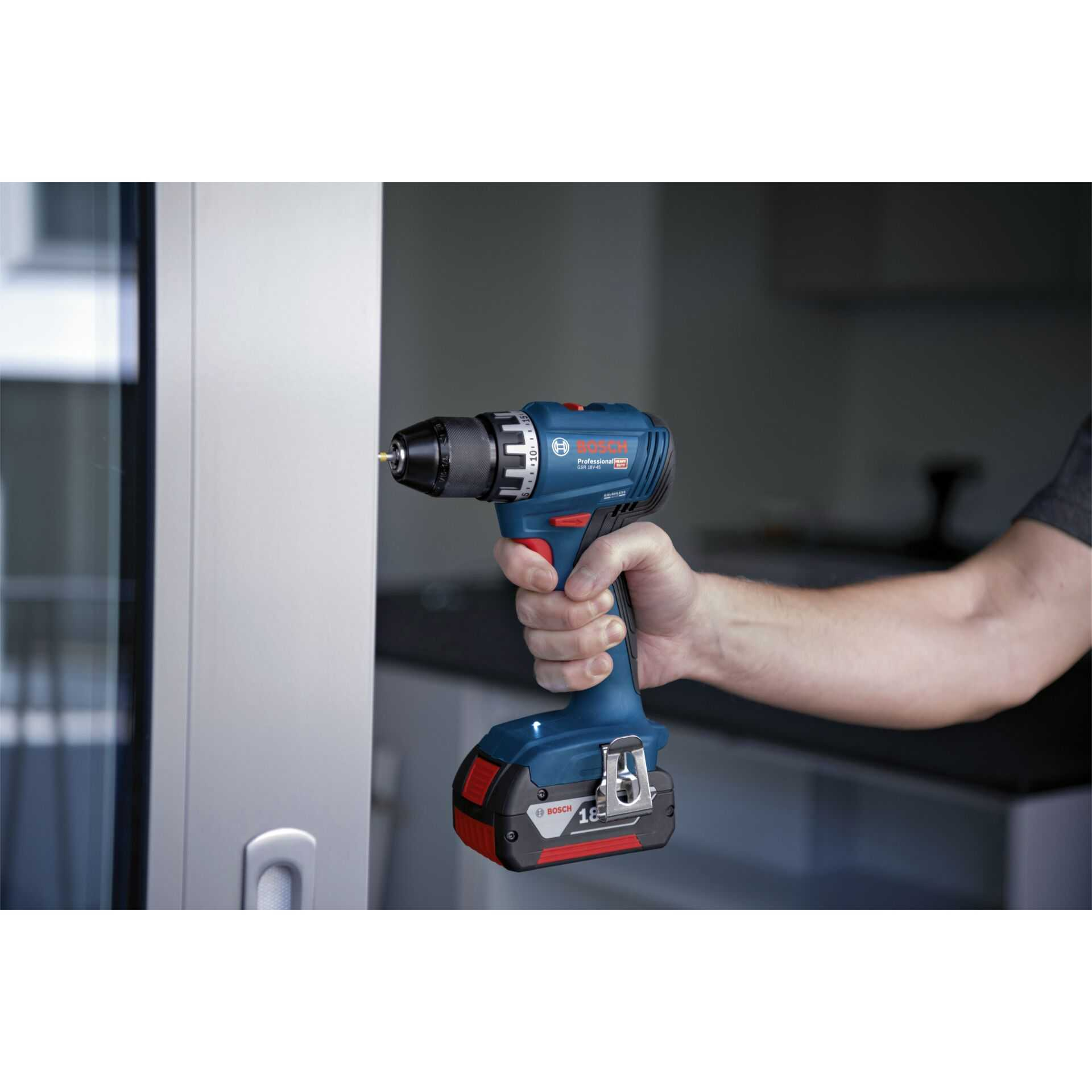 Ein Mann hält eine blaue Bosch Bohrmaschine mit einem Bohrer in einer Tür.