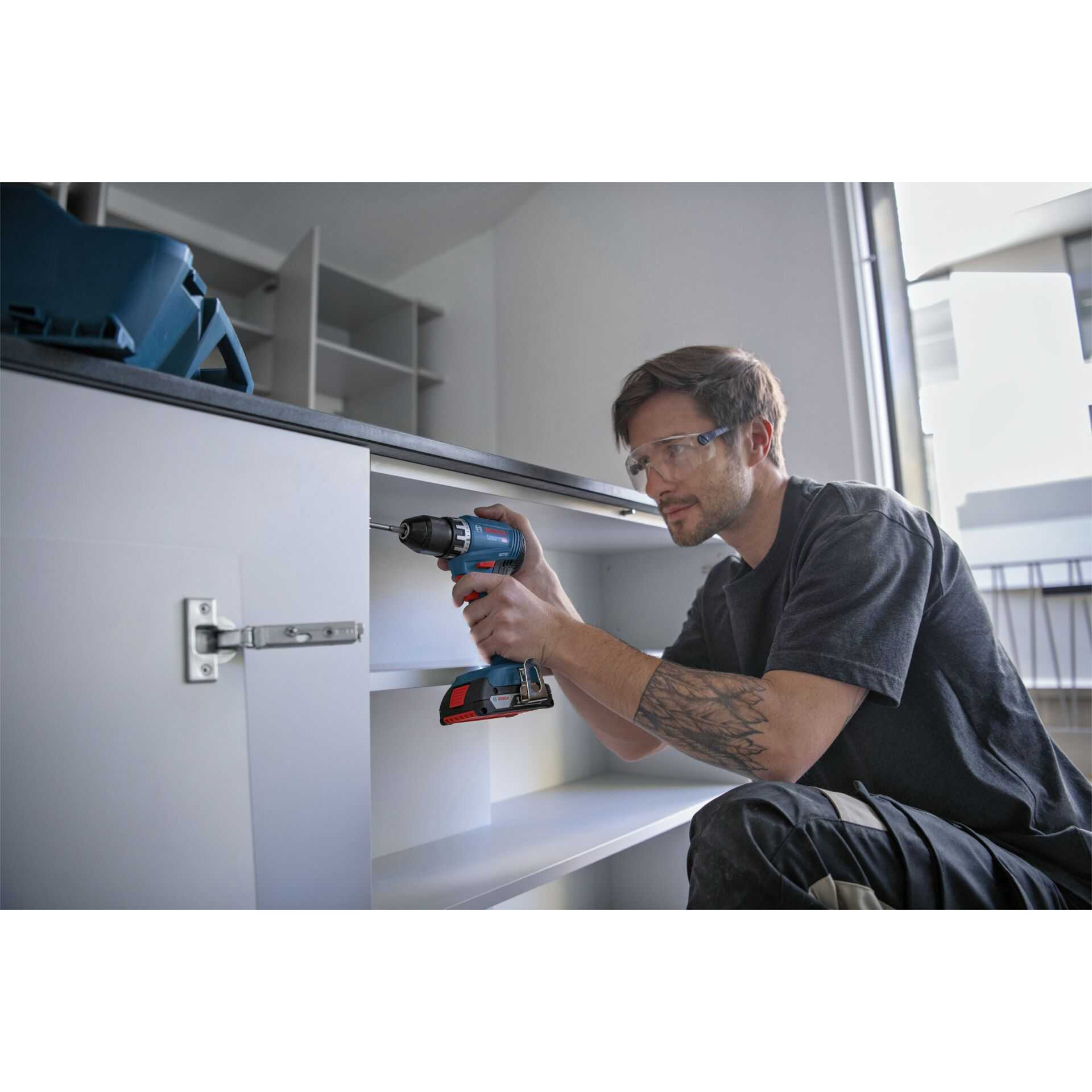 Mann mit Schutzbrille schraubt mit Akkuschrauber an einem Schrank.