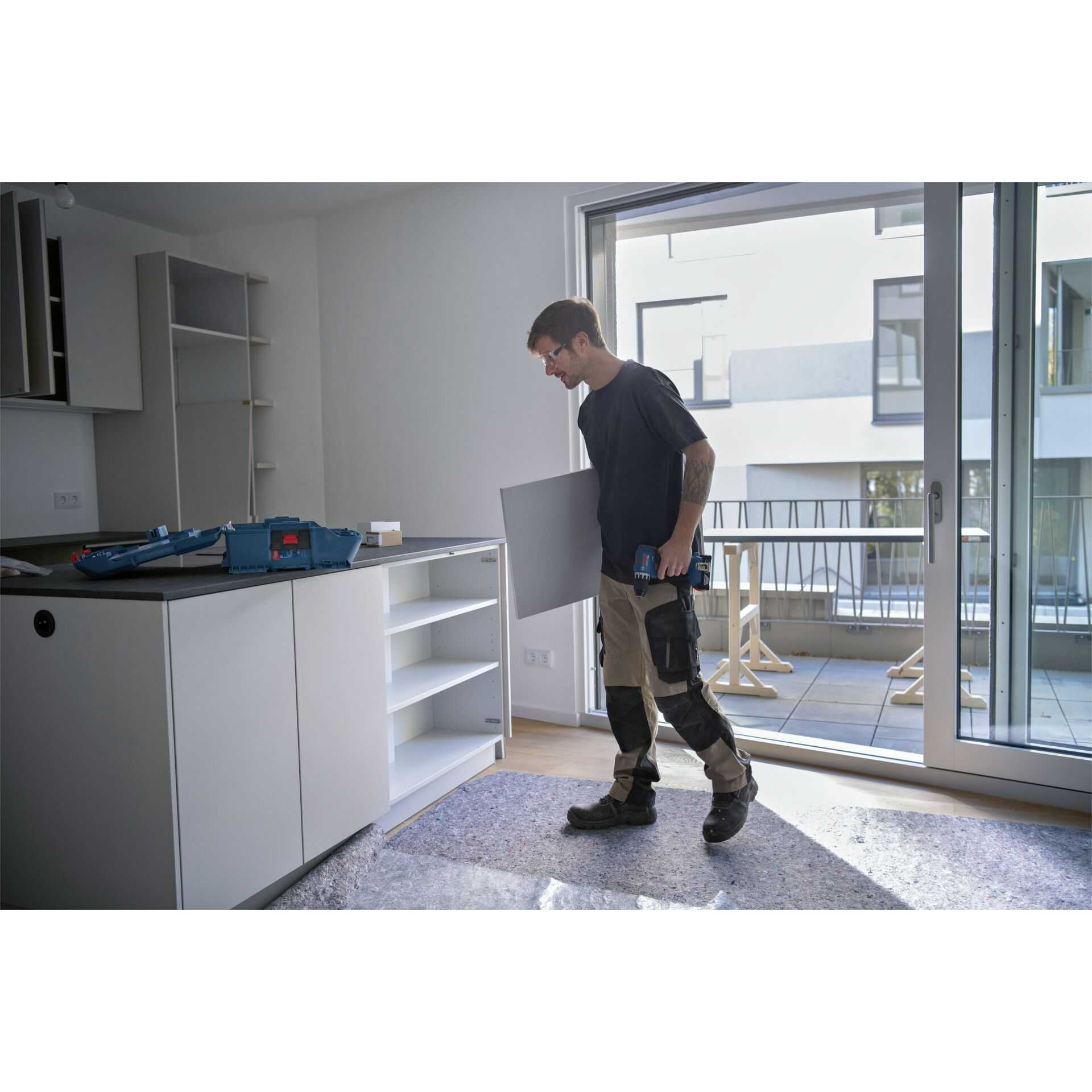 Mann mit Werkzeugkasten und Bohrer trägt Platte in Küche.