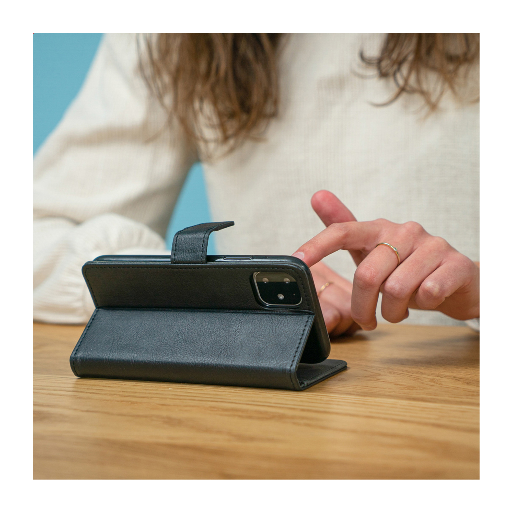 Une personne touche un étui de téléphone noir ouvert sur une table en bois.