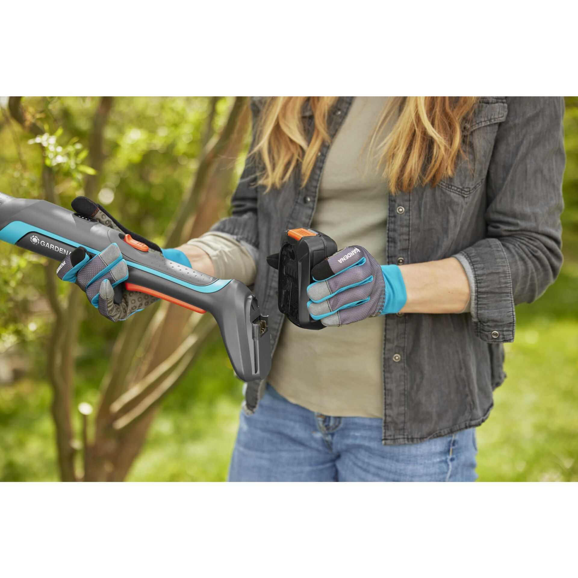 Eine Person in Gartenhandschuhen hält einen Rasentrimmer und einen Akku.