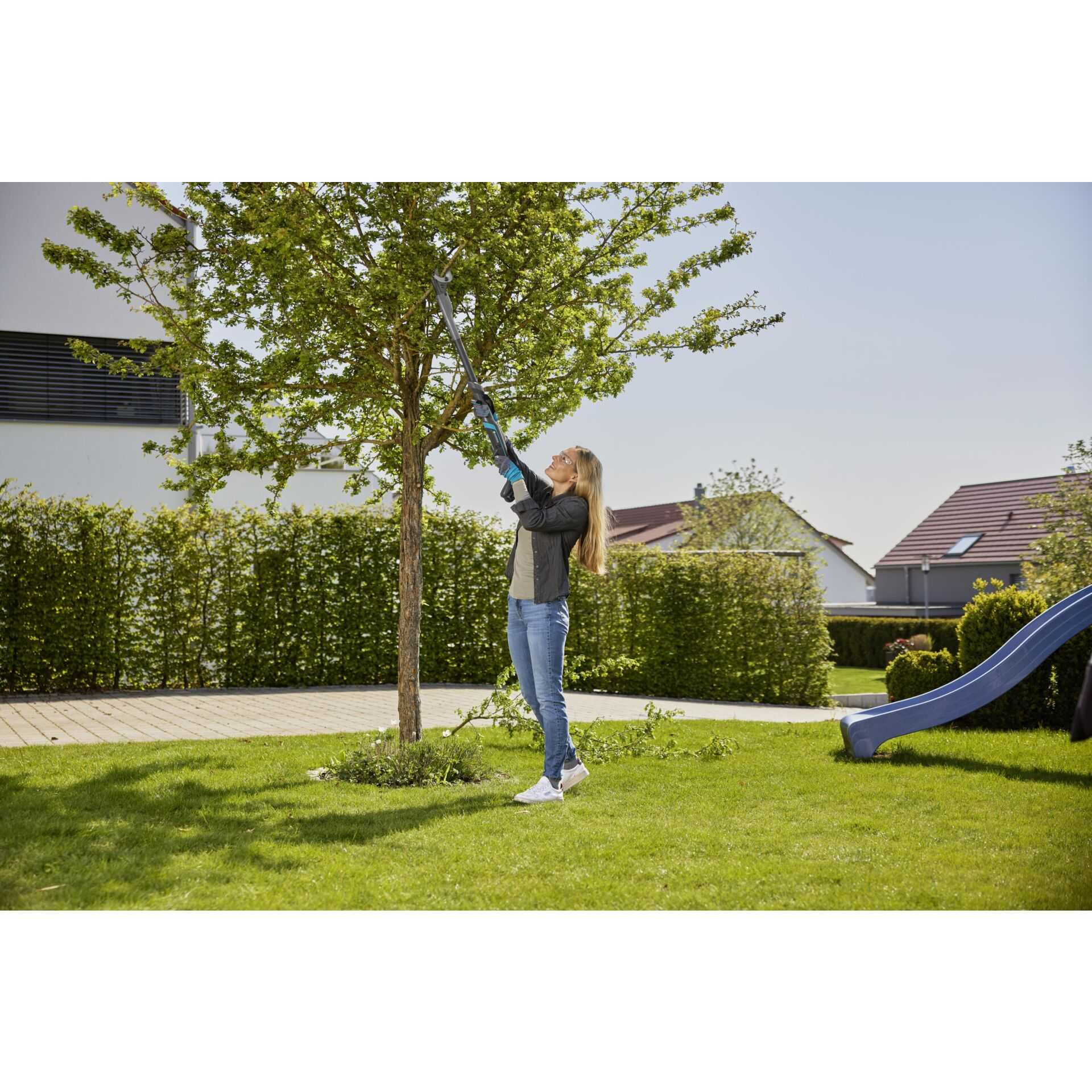 Frau schneidet Baum mit Astschere in einem Garten mit Rutsche.