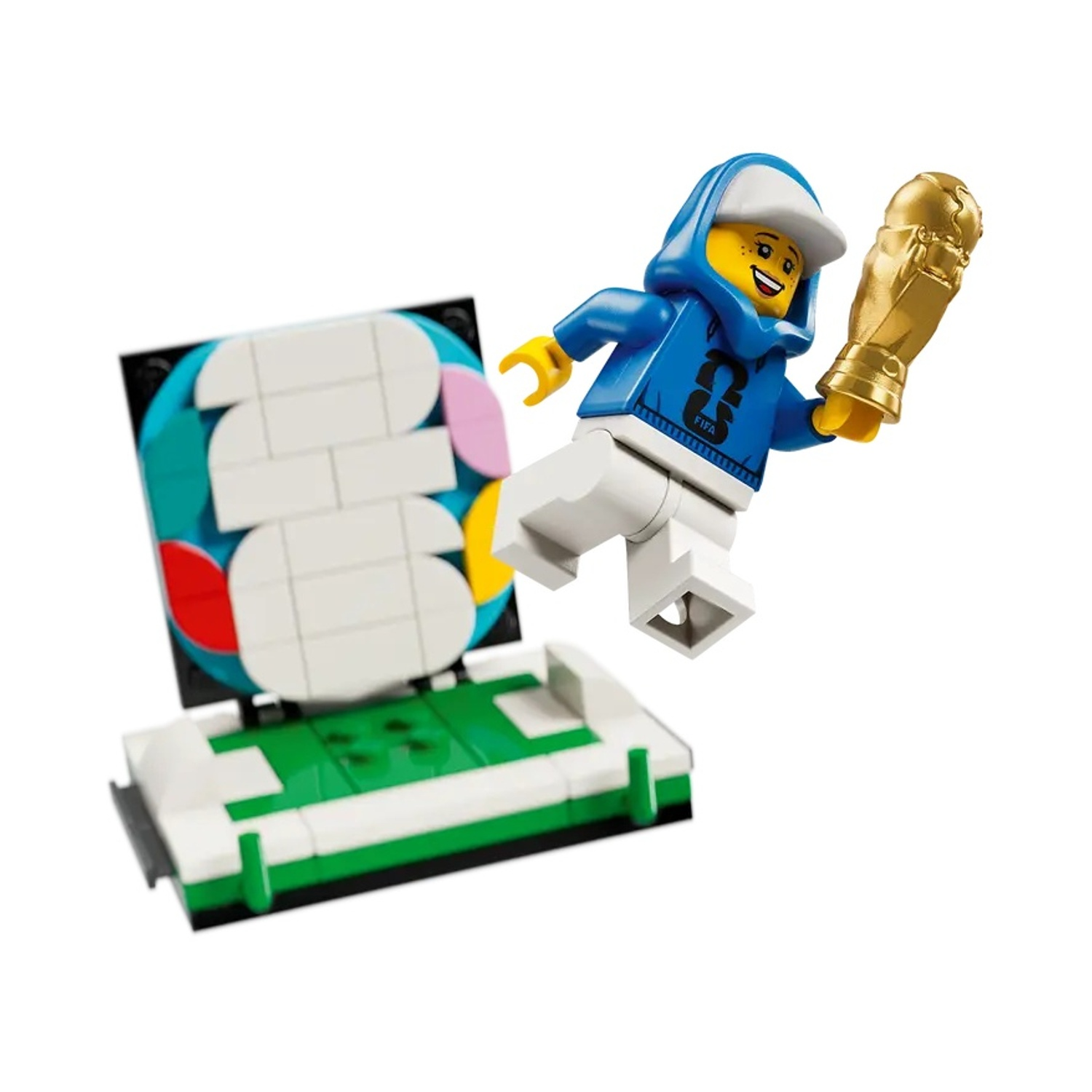 Lego figuur met beker op voetbalveld-podium met kleurrijke blokken.