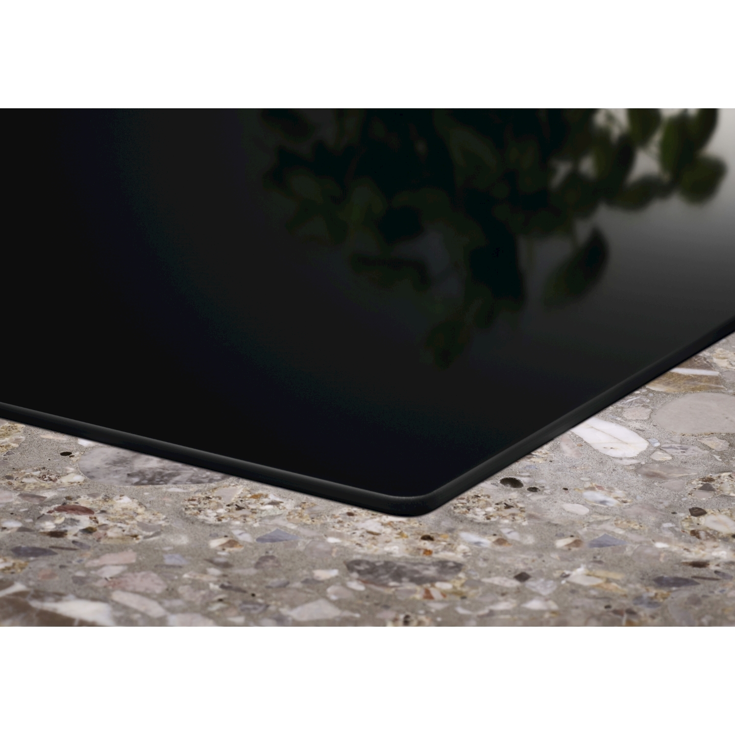 Czarna płyta indukcyjna na blacie z terakoty z odbiciami liści.