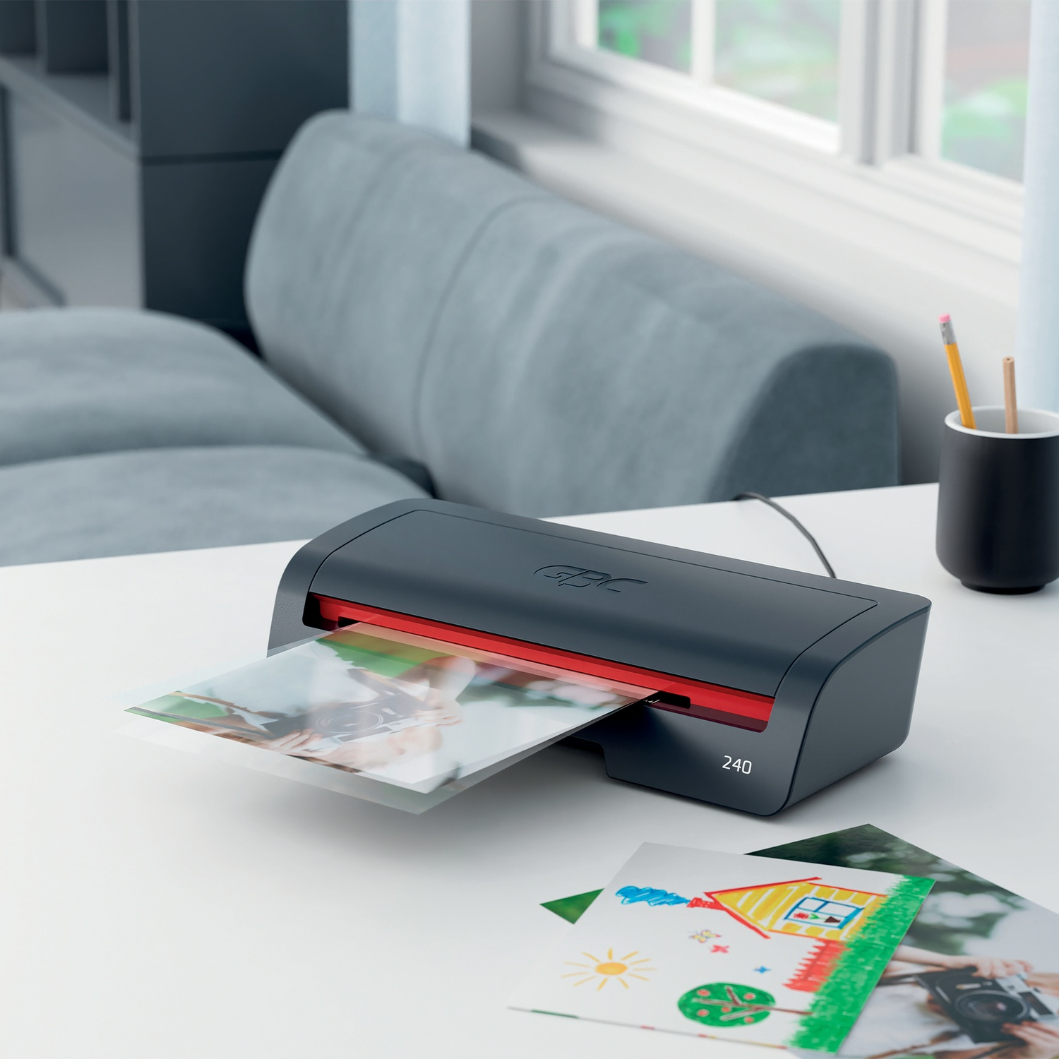 Ein schwarzer Laminator verarbeitet ein Foto, daneben liegen Kinderzeichnungen.