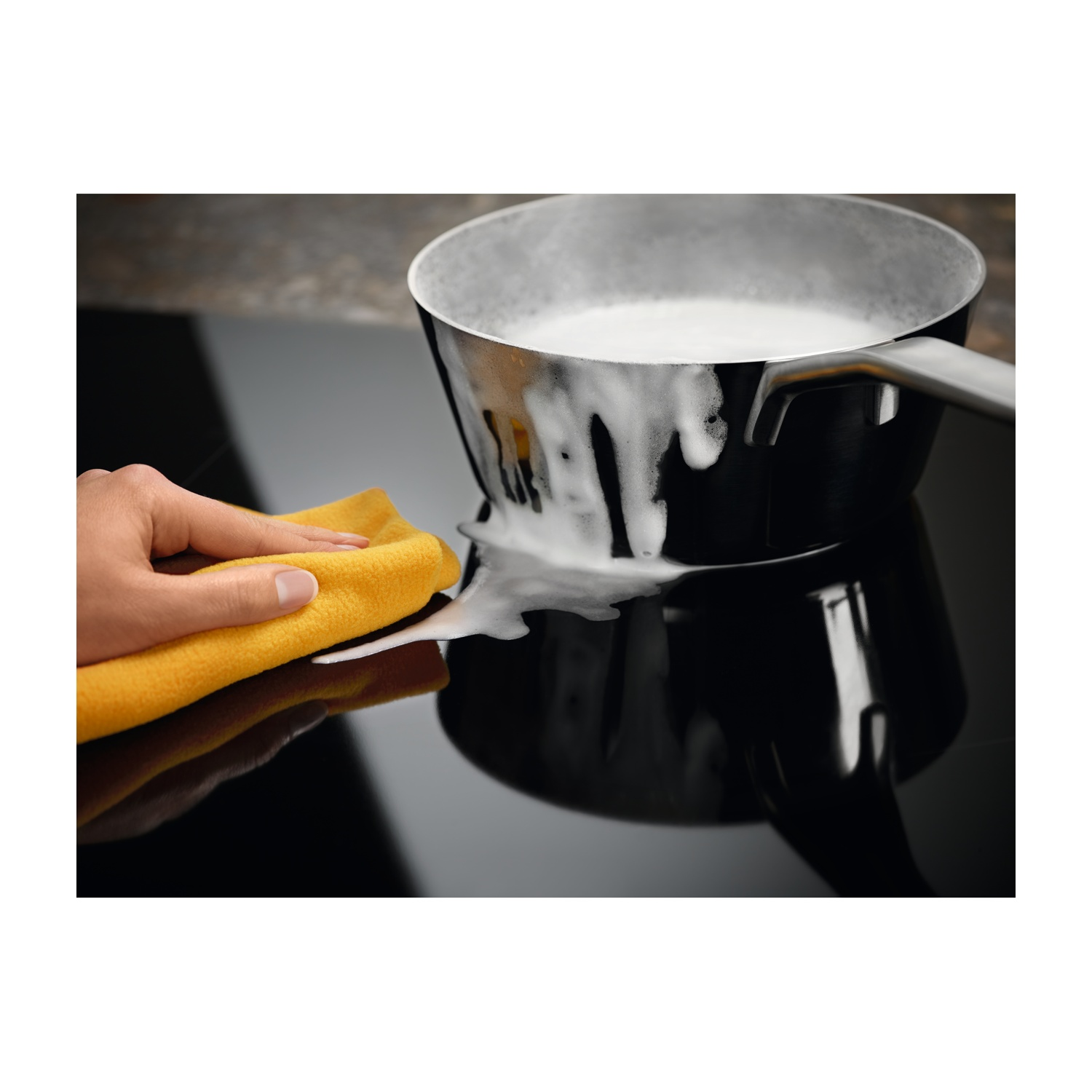 Ręka czyści czarną kuchenkę pianą za pomocą żółtej ściereczki.