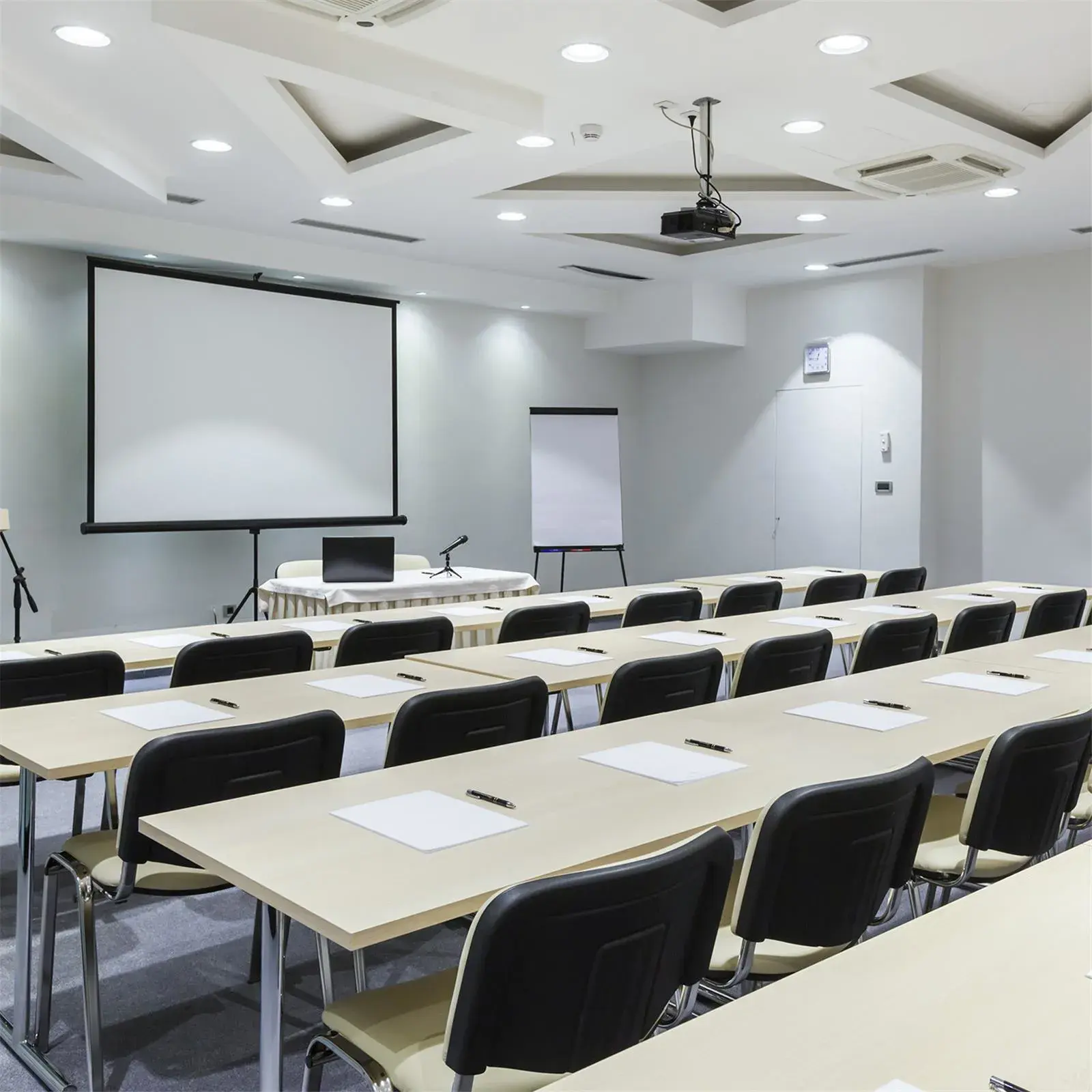 Een vergaderruimte met rijen tafels en stoelen, een projector en een scherm.