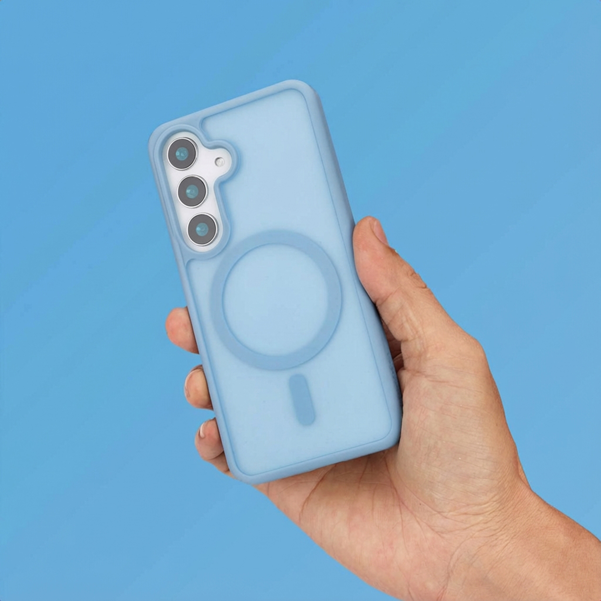 Una mano tiene una cover per telefono azzurra con tre fotocamere. Sfondo luminoso.