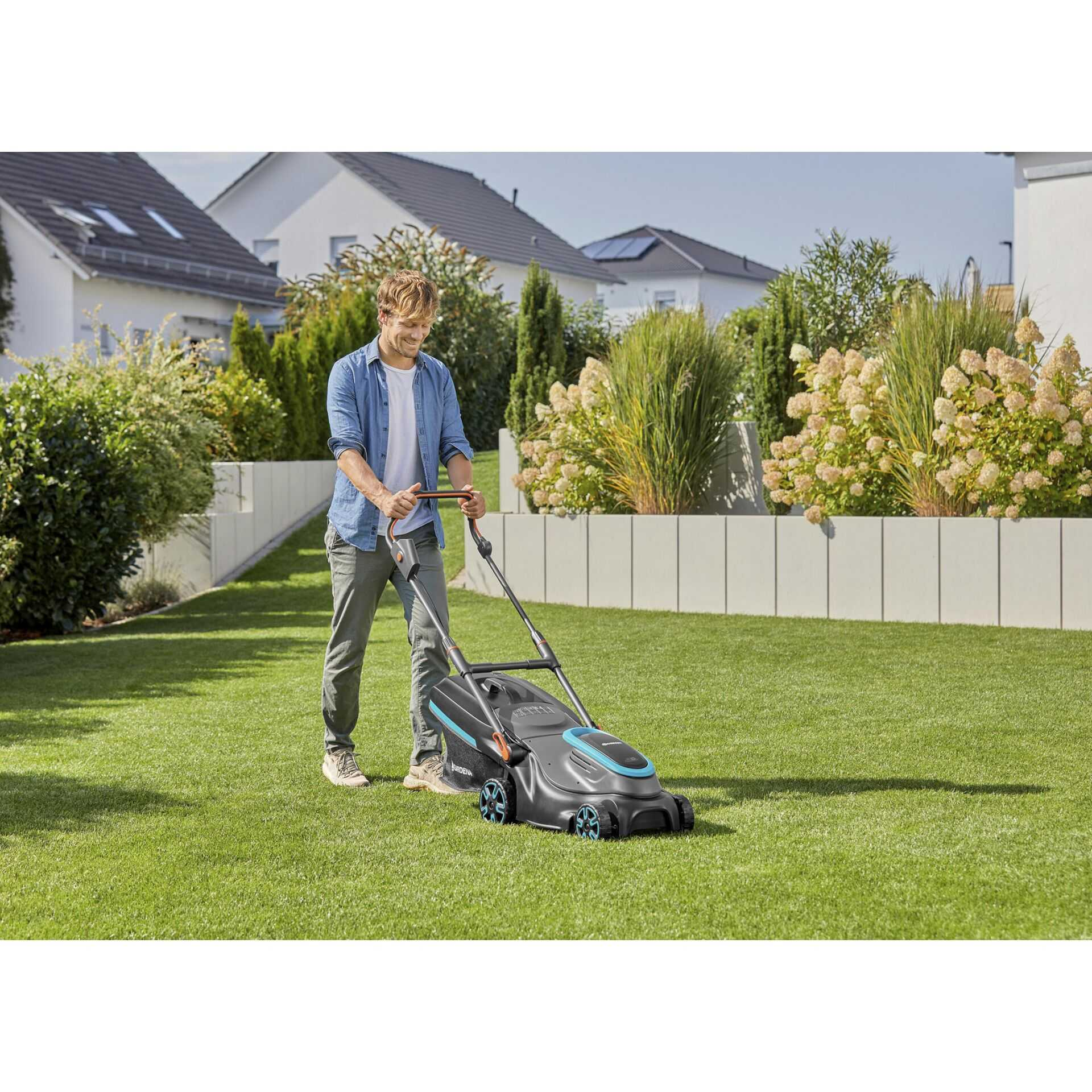 Mann mäht Rasen mit einem Rasenmäher in einem gepflegten Garten mit Häusern.