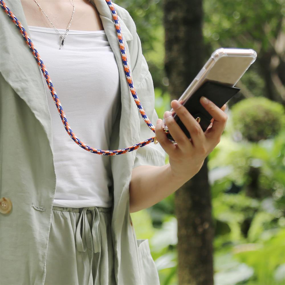 Una persona tiene uno smartphone con un cordino in un ambiente verde all'aperto.